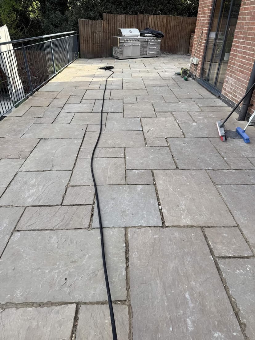 Large sandstone patio mid-clean — the wet stone showing the colour coming back.